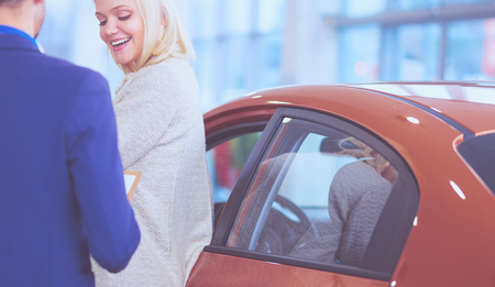 Dealer with woman stands near a new car in the showroomの写真素材