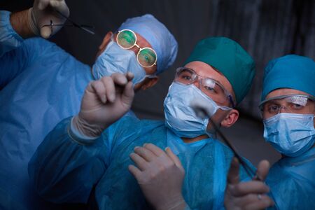 Group of surgeons at work in operating theater toned in blue. Medical team performing operationの写真素材