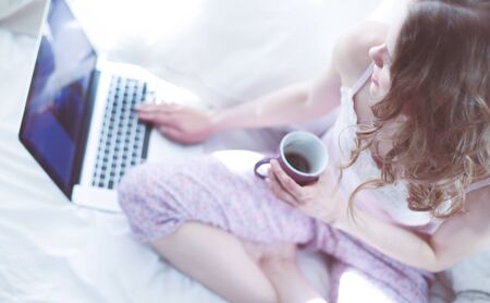 Young beautiful woman sitting in bed with laptop.の写真素材