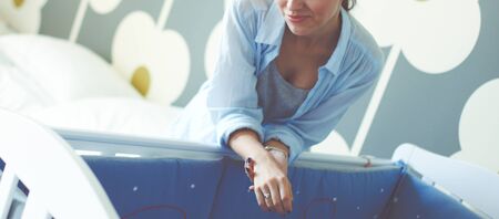 Young woman standing near childrens cot. Young momの写真素材