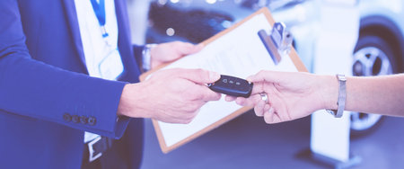 Car salesman sells a car to happy customer in car dealership and hands over the keys.