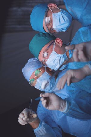 Group of surgeons at work in operating theater toned in blue. Medical team performing operationの写真素材
