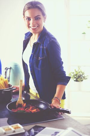 Young woman cooking healthy food holding a pan with vegetables is it. Healthy lifestyle, cooking at home conceptの写真素材