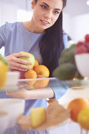 Smiling woman taking a fresh fruit out of the fridge, healthy food conceptの写真素材
