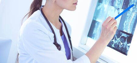 Young smiling female doctor with stethoscope pointing at X-ray at doctors officeの写真素材