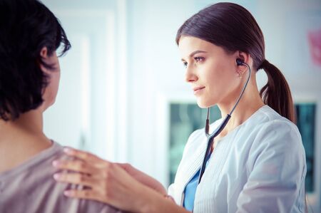 A female doctor listening a patient with a stethoscopeの写真素材