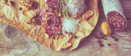 Italian salami wih sea salt, rosemary, garlic and nuts on paper. Rustic style. Top view.