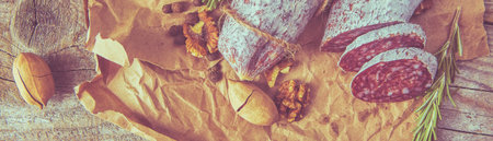 Italian salami wih sea salt, rosemary, garlic and nuts on paper. Rustic style. Close up.