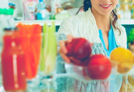 Portrait of female standing near open fridge full of healthy food, vegetables and fruits. Portrait of femaleの写真素材