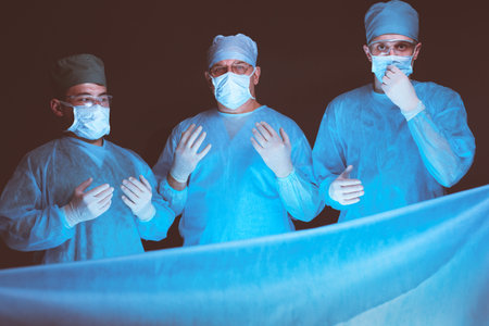 Group of surgeons at work in operating theater toned in blue. Medical team performing operation