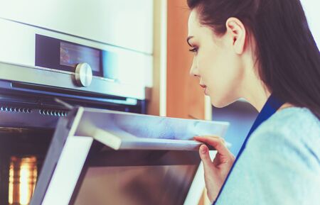 Beautiful young woman checking how her cake is doing in the ovenの写真素材