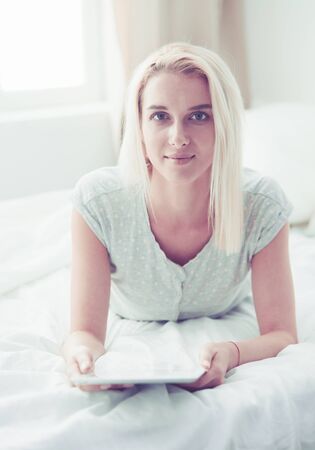 Girl holding digital tablet with blank screen and smiling at camera in bedroomの写真素材