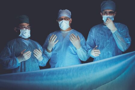 Group of surgeons at work in operating theater toned in blue. Medical team performing operationの写真素材