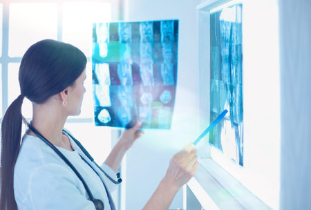 Young smiling female doctor with stethoscope pointing at X-ray at doctors office