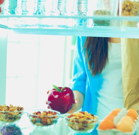 Portrait of female standing near open fridge full of healthy food, vegetables and fruits.の写真素材