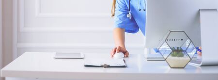 Portrait of female physician using laptop computer while standing near reception desk at clinic or emergency hospitalの写真素材