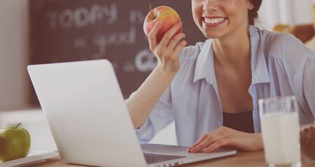Woman with apple and laptop sitting in the kitchenの写真素材
