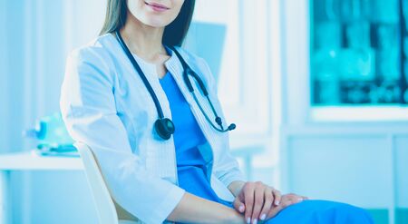 Beautiful female doctor sitting in a consulting room, smiling at the cameraの写真素材