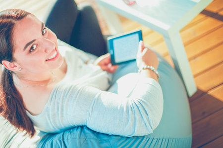 Smiling young woman sitting on sofa with touchpad.