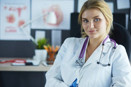 Beautiful young smiling female doctor sitting at the deskの写真素材