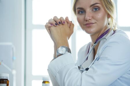 Beautiful young smiling female doctor sitting at the deskの写真素材