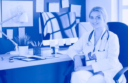 Portrait of young female doctor sitting at desk in hospitalの写真素材