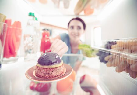 Portrait of female standing near open fridge full of healthy food, vegetables and fruits.の写真素材