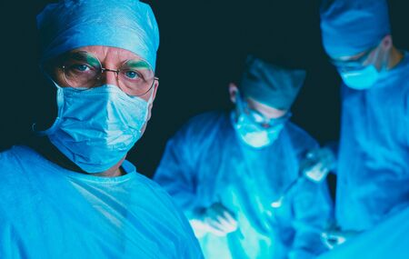 Group of surgeons at work in operating theater toned in blue. Medical team performing operation.の写真素材
