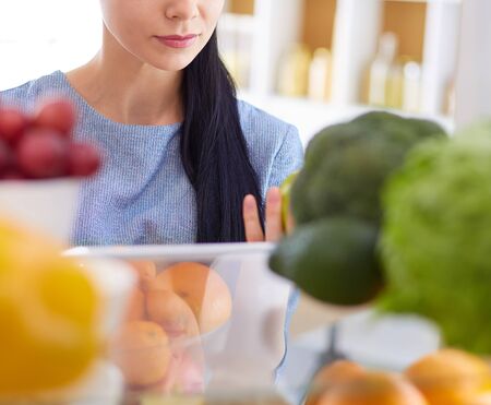 Smiling woman taking a fresh fruit out of the fridge, healthy food concept.の写真素材