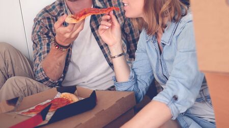 Young couple have a pizza lunch break on the floor after moving into a new home with boxes around them. Young coupleの写真素材