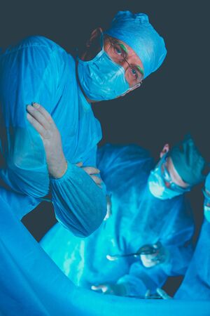 Group of surgeons at work in operating theater toned in blue. Medical team performing operationの写真素材