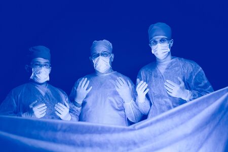 Group of surgeons at work in operating theater toned in blue. Medical team performing operationの写真素材