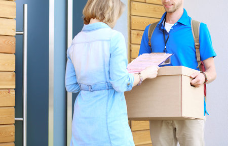 Smiling delivery man in blue uniform delivering parcel box to recipient - courier service concept....