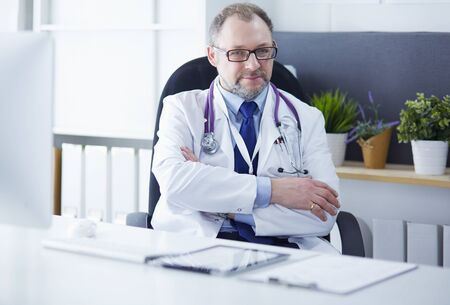 Portrait of senior doctor in office sitting at the deskの写真素材