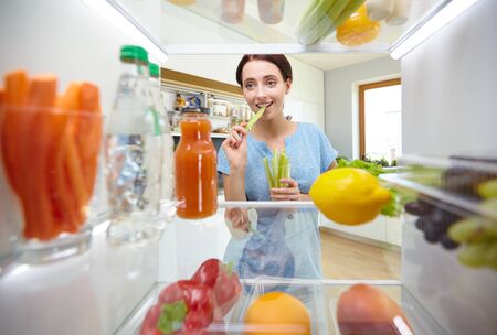 Young woman taking fresh healthy vegetables from the fridge and preparing lunch, diet and lifestyle conceptの写真素材