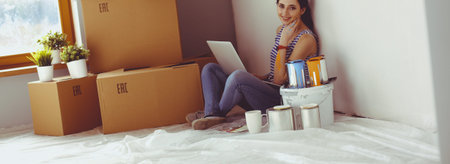 Young woman portrait while painting new apartment ,sitting with laptop