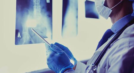 Doctor in hospital sitting at desk looking at x-rays on tablet against white background with x-rays.の写真素材