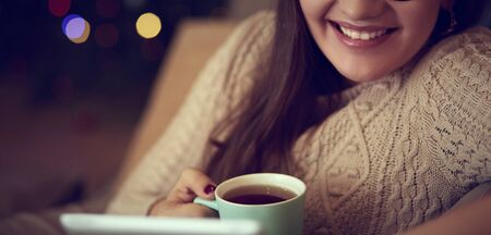 Young pretty woman having coffee and using laptop computer on sofa at home.の写真素材