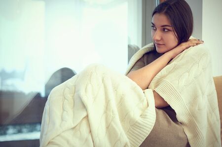 Young woman in plaid sitting on windowsillの写真素材