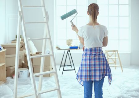 Beautiful young woman doing wall painting, standing near ladder.の写真素材