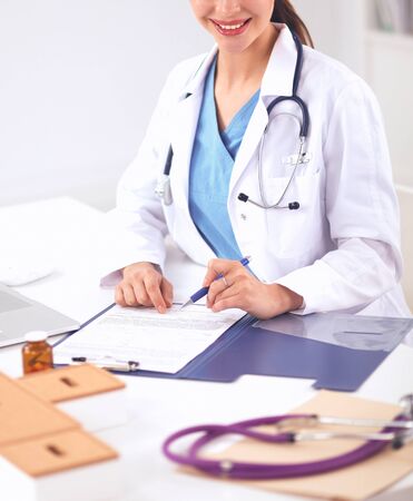 Beautiful young smiling female doctor sitting at the desk and writing.の写真素材