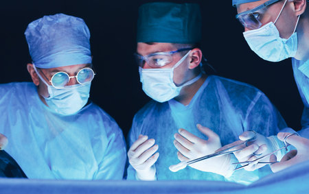 Group of surgeons at work in operating theater toned in blue. Medical team performing operation.