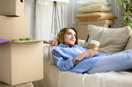 Happy young woman lying on sofa at new home , drinking coffee or tea