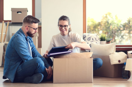 Happy couple looking at photo album while unpacking stuff after relocation to new flat