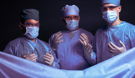 Group of surgeons at work in operating theater toned in blue. Medical team performing operation