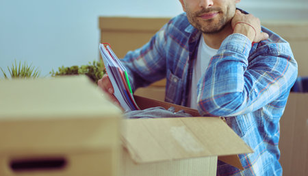 A moving man sitting on the floor in empty apartment, Among the Boxes, Checking the List of Things