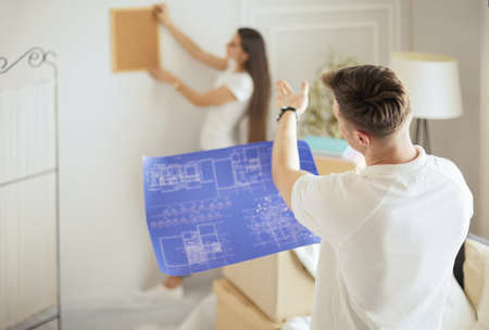 Woman helps her partner to hang painting on wall of their new house, she is framing the photo with her fingers.の写真素材