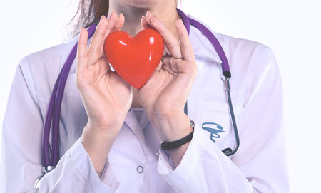 Young woman doctor holding a red heart, isolated on white background