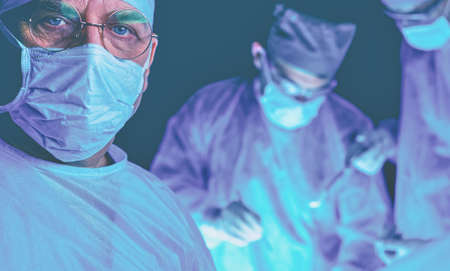 Group of surgeons at work in operating theater toned in blue. Medical team performing operationの写真素材