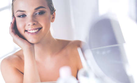 Young woman in bathrobe looking in bathroom mirrorの写真素材